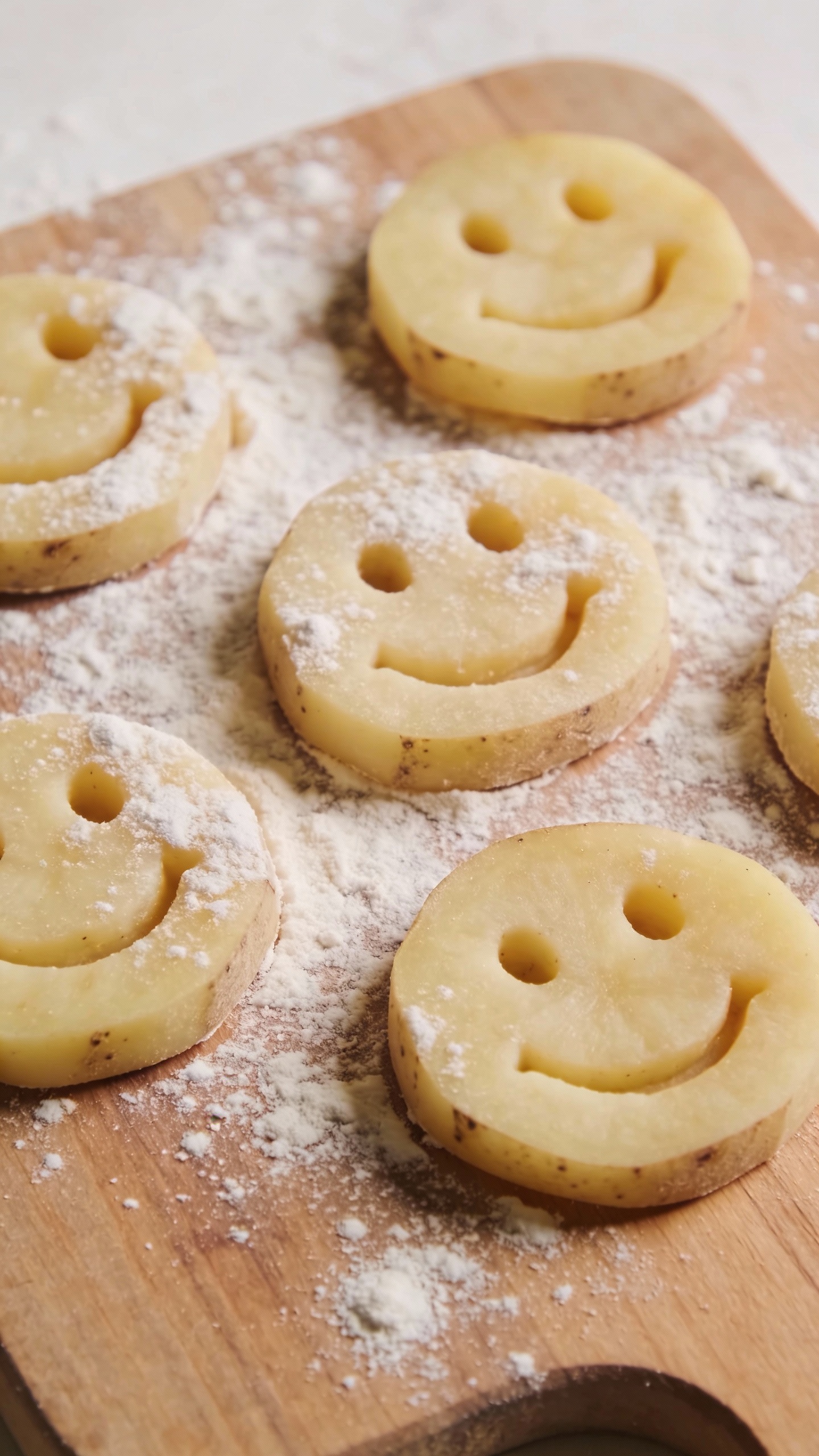 uncooked potato smiley shapes on floured board, top-down