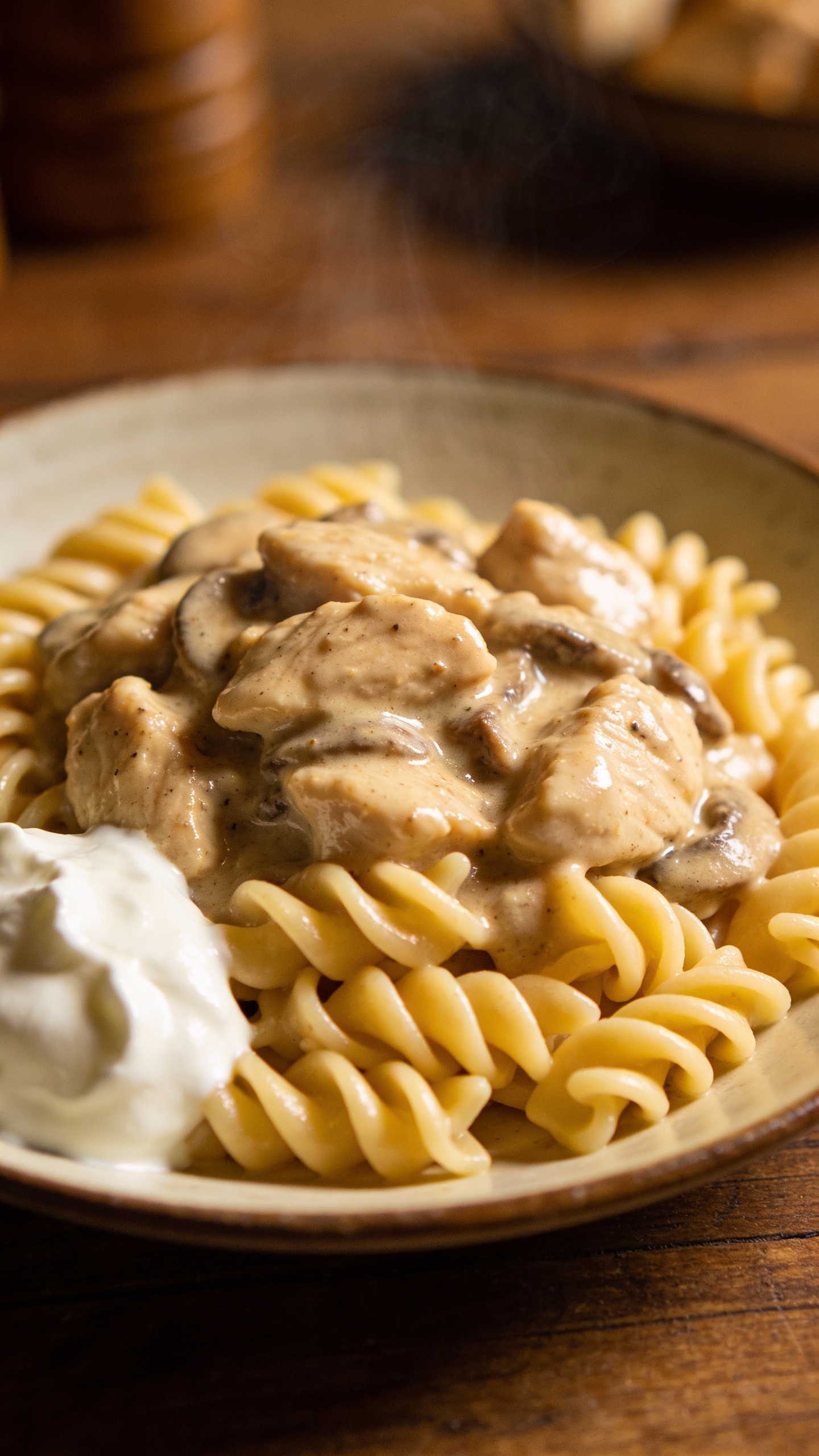 Twirled egg noodles topped with chicken stroganoff, sour cream dollop