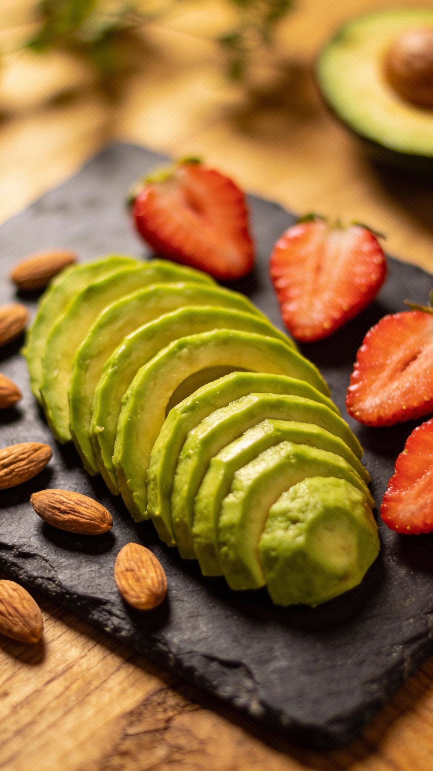Sliced avocado, almonds, strawberries on slate board