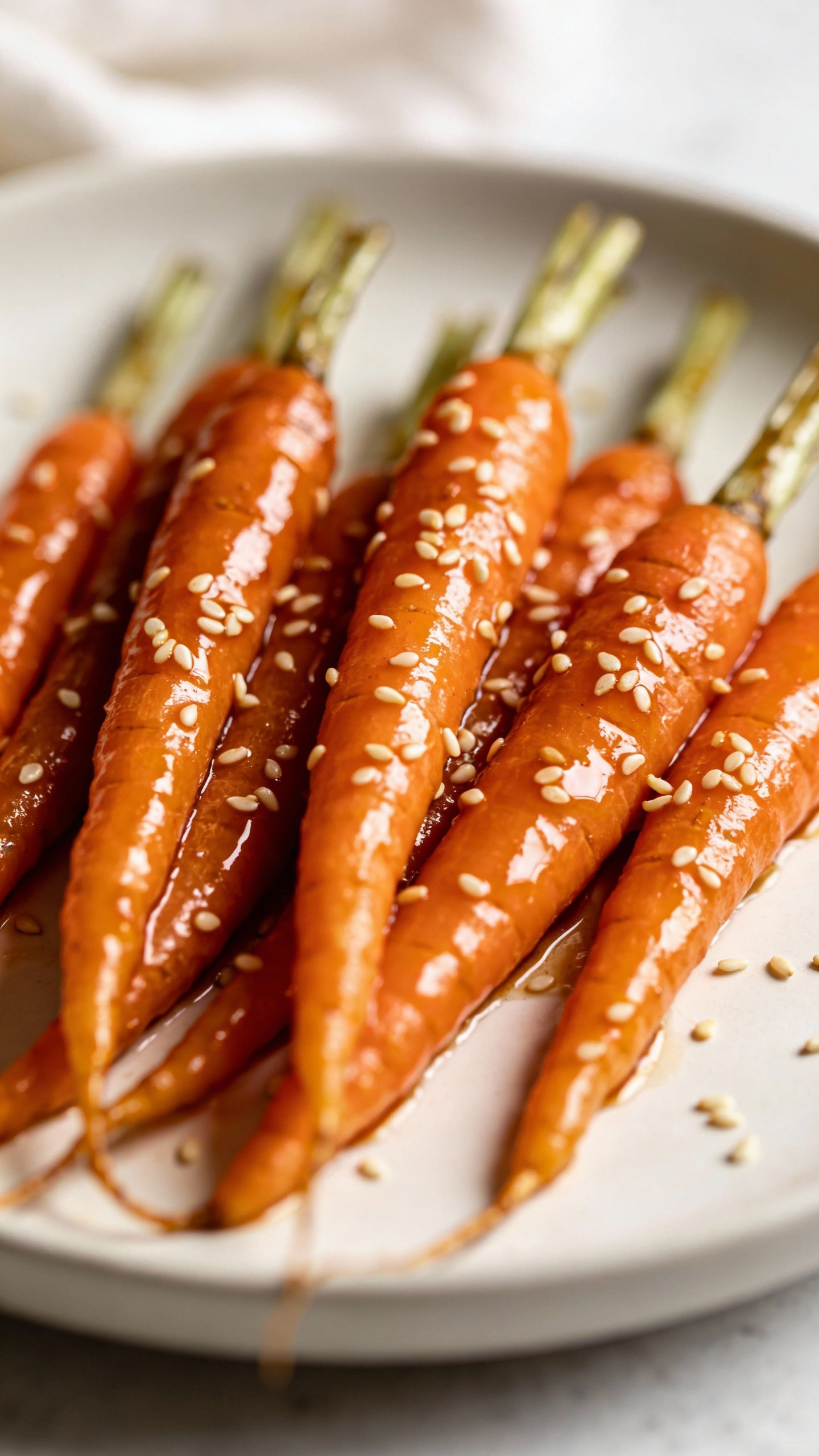 glossy honey-garlic carrots on white plate, sesame sprinkle