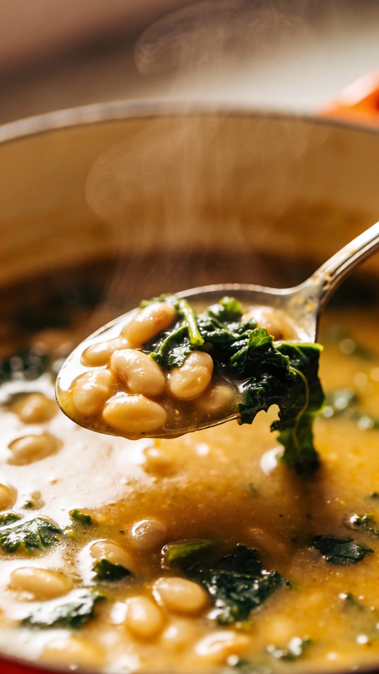 Close-up spoonful of white bean kale soup, steam rising