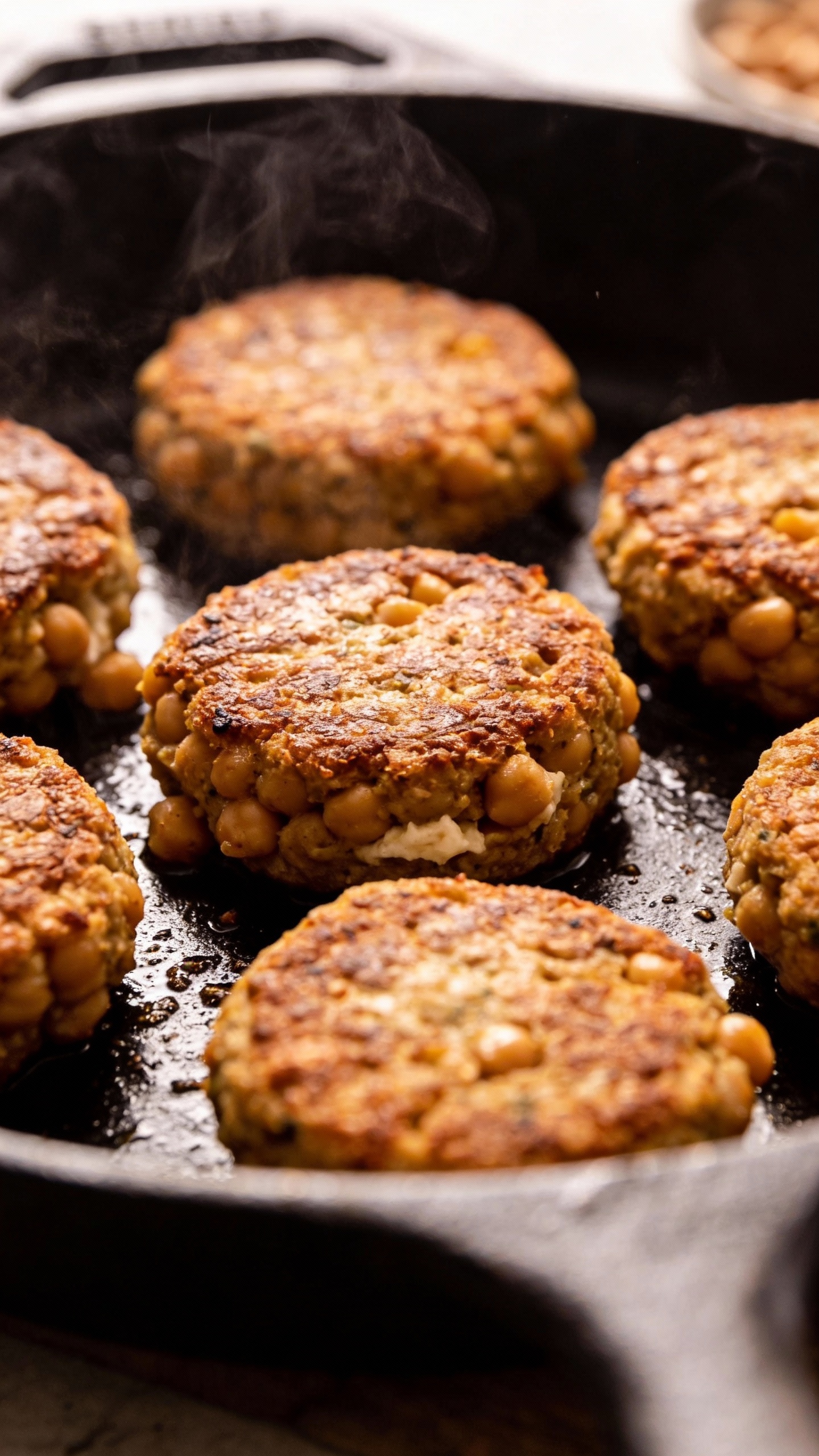 pan-seared chickpea patties in cast-iron skillet, steam