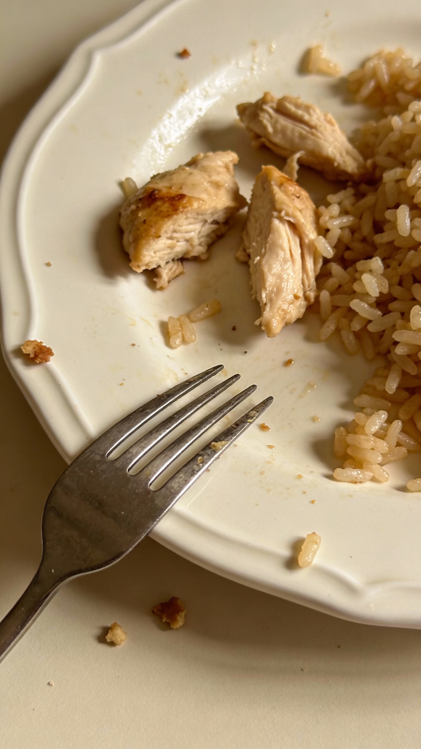 leftover chicken and rice on white plate, silver fork, crumbs