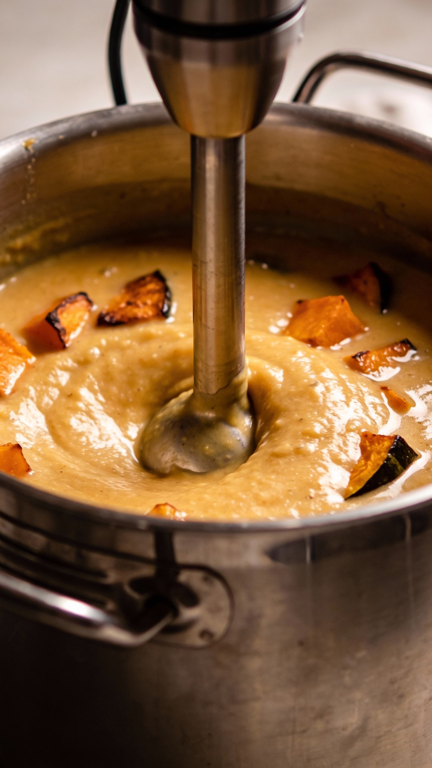 Immersion blender puréeing roasted veggie soup, stainless pot