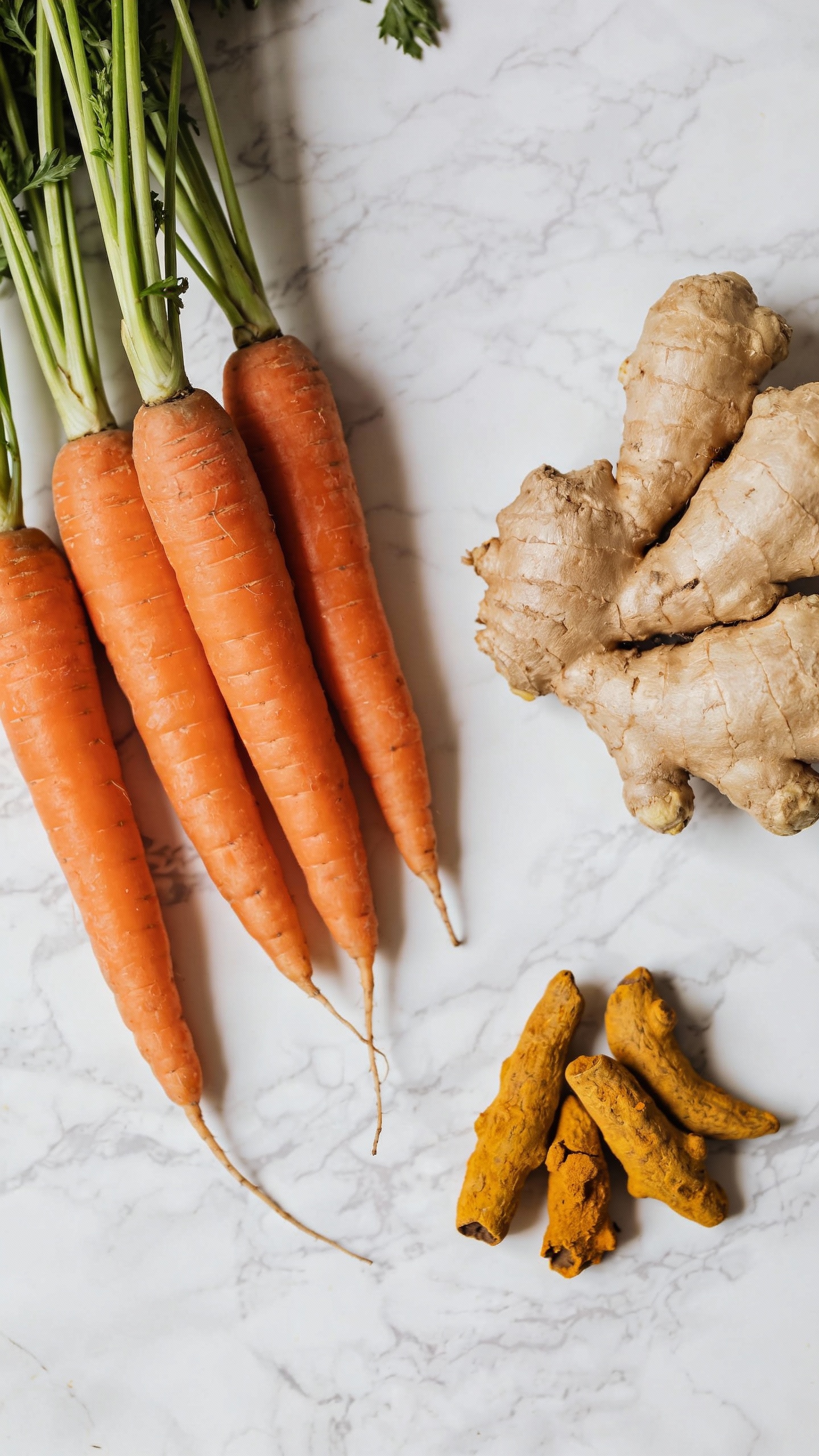 Fresh carrots, ginger, and turmeric on marble, overhead shot