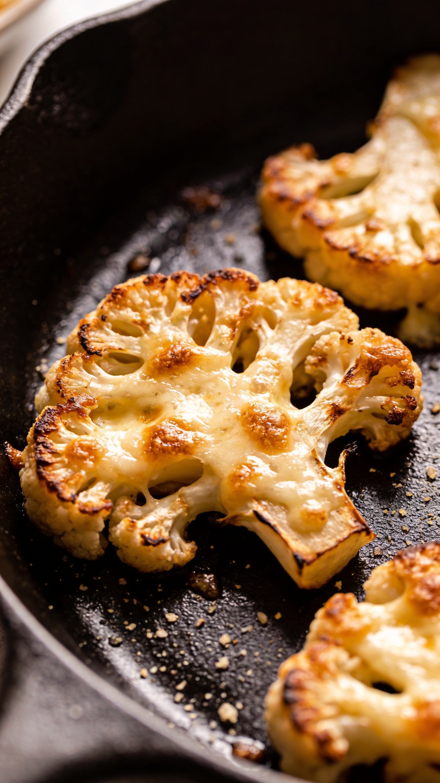 cheesy cauliflower steaks on cast-iron skillet, crisp edges