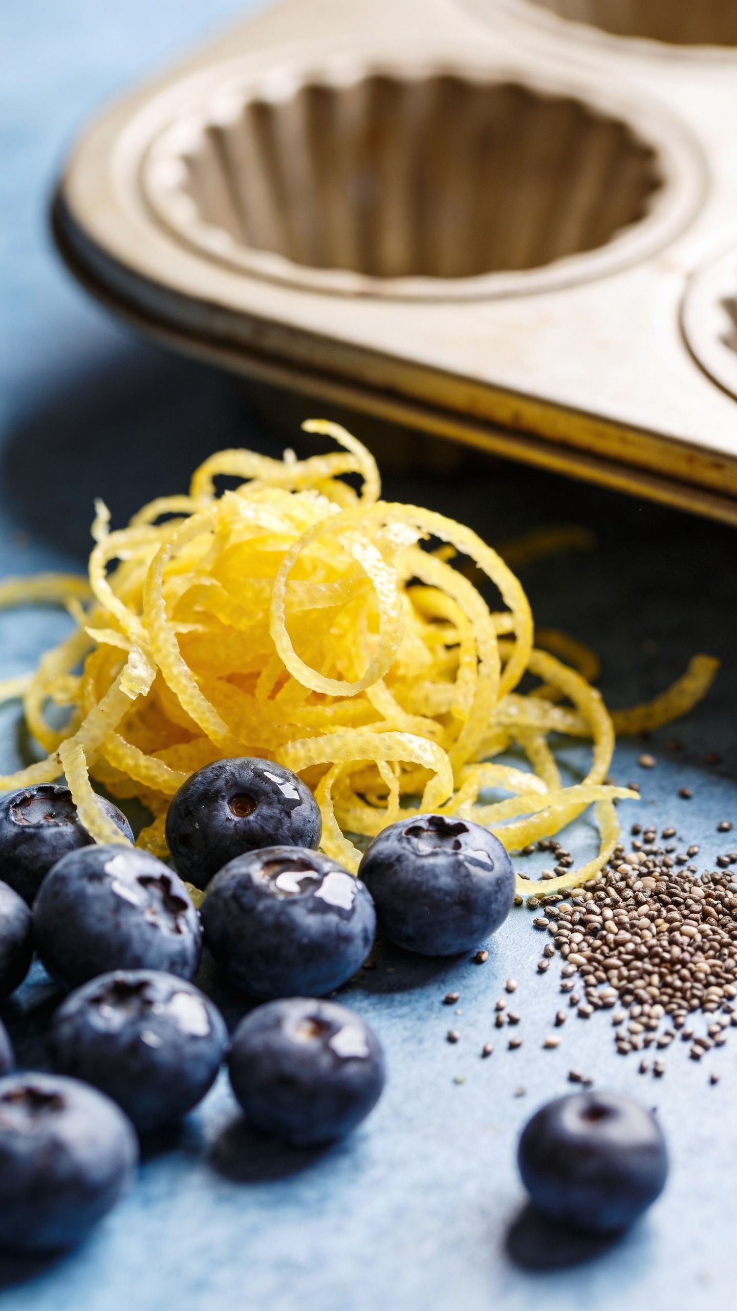 Fresh lemon zest, blueberries, and poppyseeds beside muffin tin