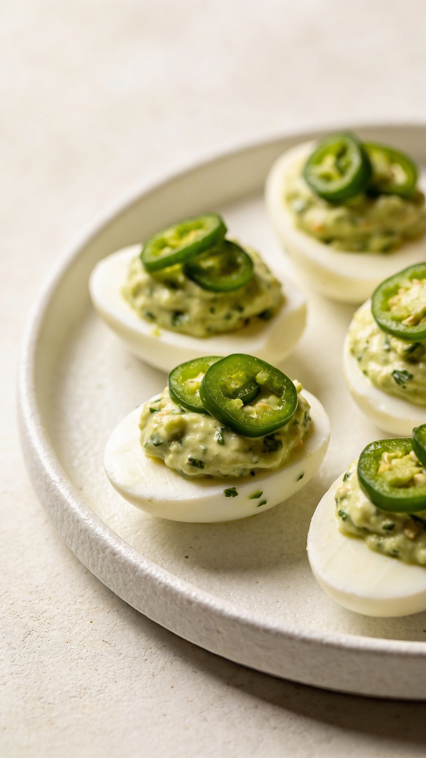 avocado-herb deviled eggs with jalapeño slices, white ceramic plate