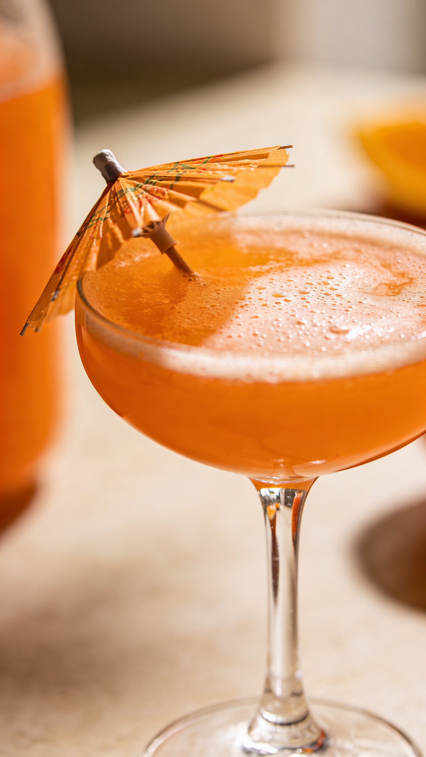 Close-up orange punch in coupe glass, tiny umbrella