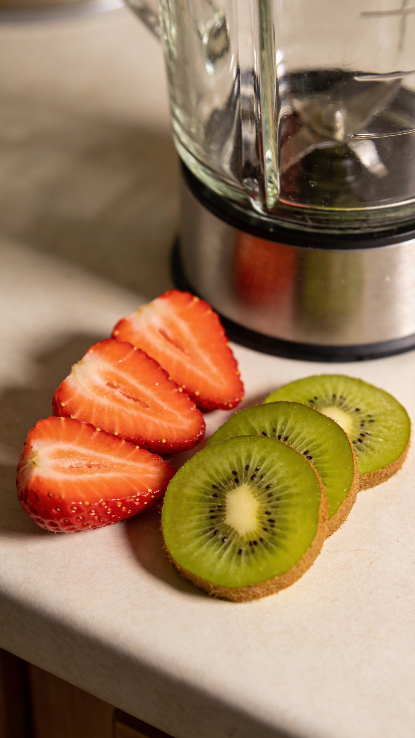 sliced strawberries and kiwis beside blender on counter