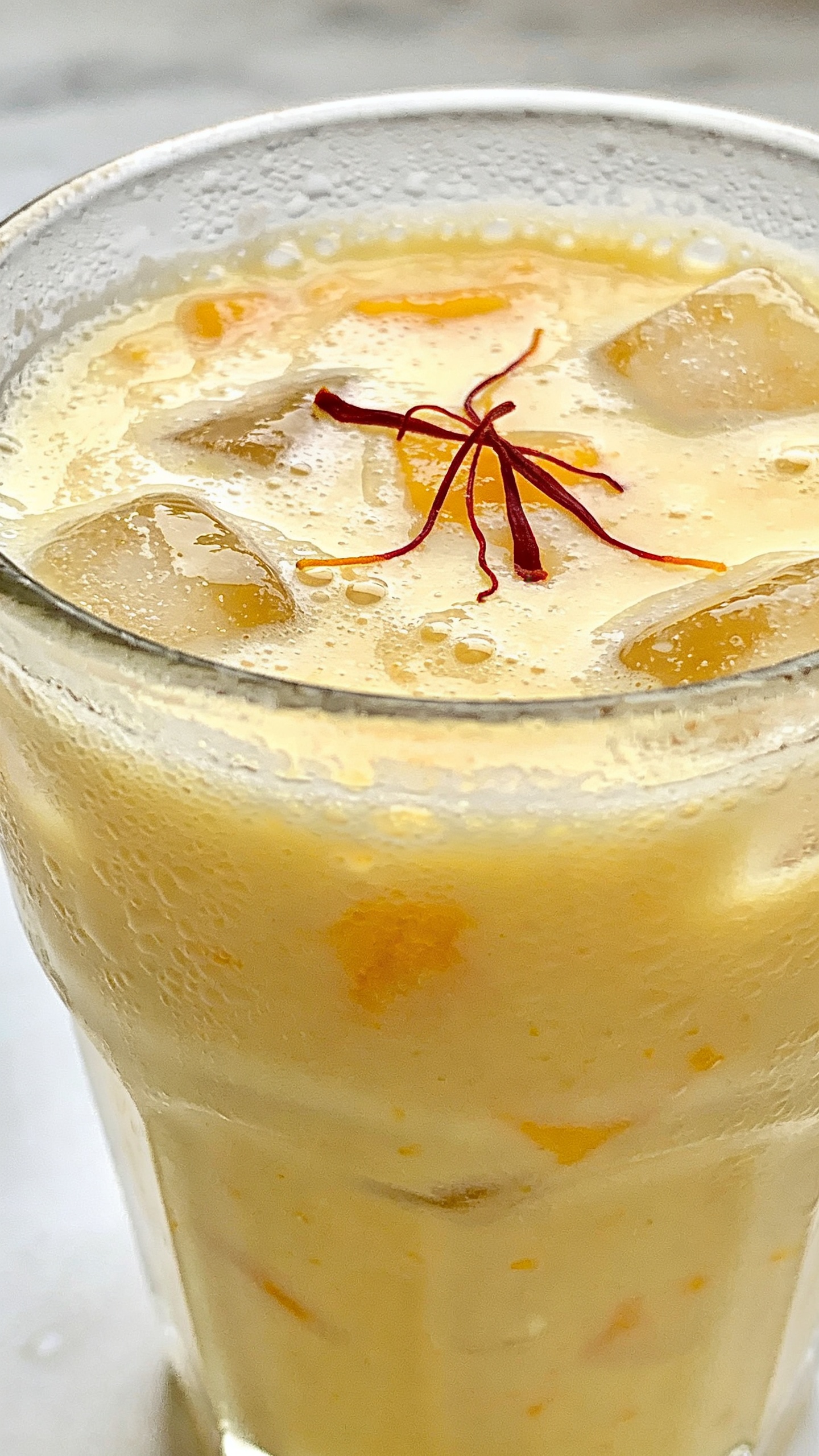 frosty mango lassi in clear glass, saffron garnish