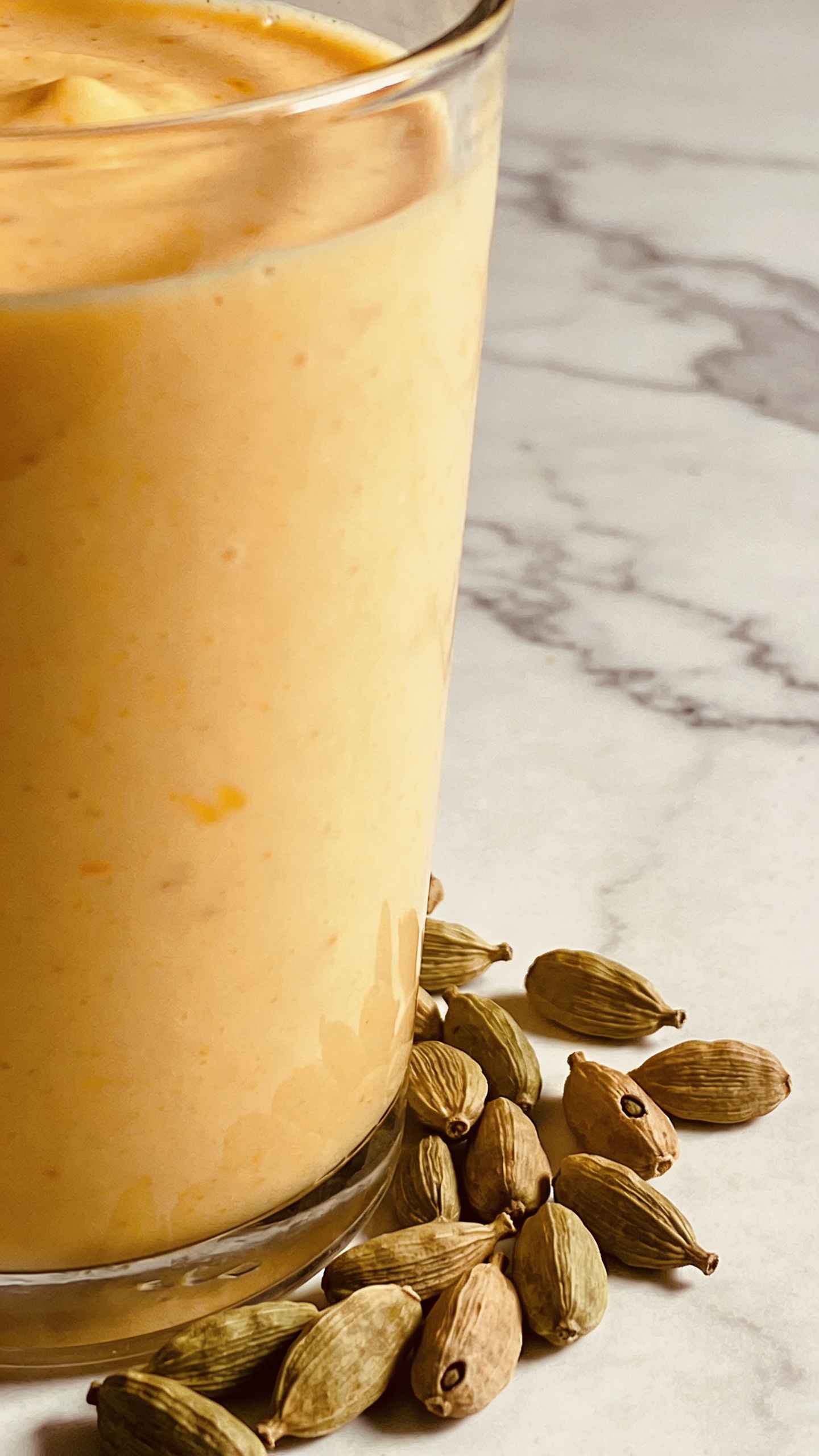 mango lassi with cardamom pods on marble background