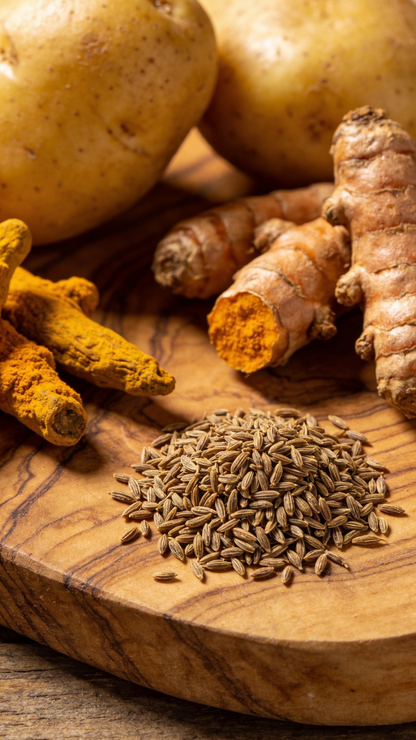 Whole cumin, turmeric, and potatoes on wooden board
